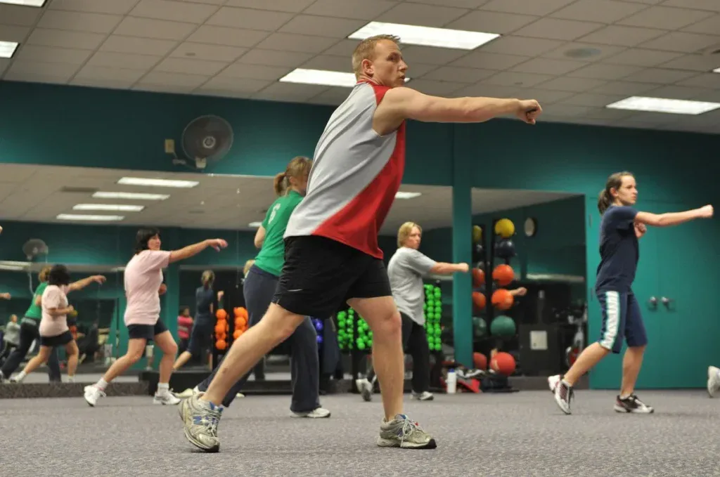 Instruktor prowadzi zajęcia fitness dla grupy na sali, kurs instruktora fitness