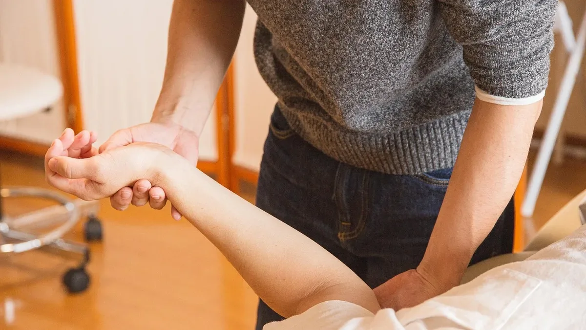 Kurs trenera medycznego: fizjoterapeuta bada ramię i nadgarstek pacjenta w gabinecie