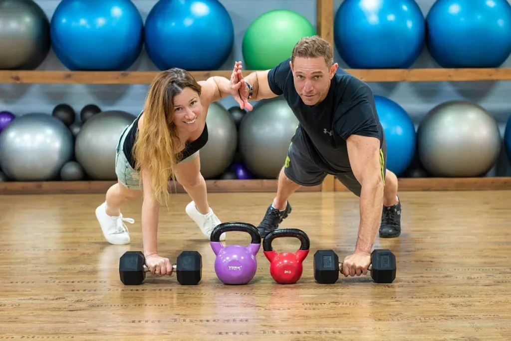 Trener i klientka w podporze przy hantlach i kettlebellach na sali fitness